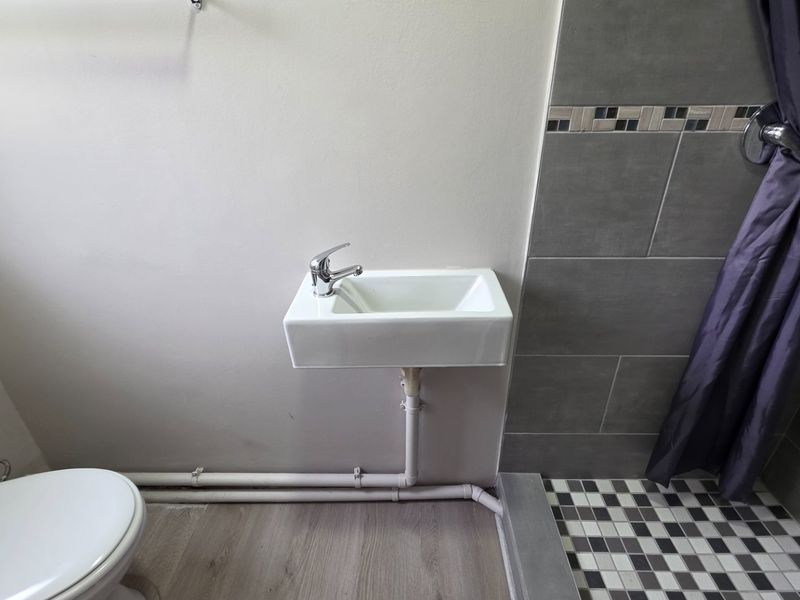 A compact bathroom featuring a wall-mounted basin, toilet, and a tiled shower area with mosaic flooring.