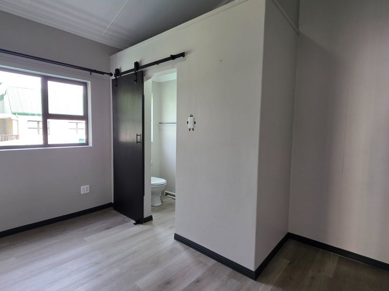 A clean, empty bedroom featuring modern laminate flooring, a sliding barn door, and an en-suite toilet area.