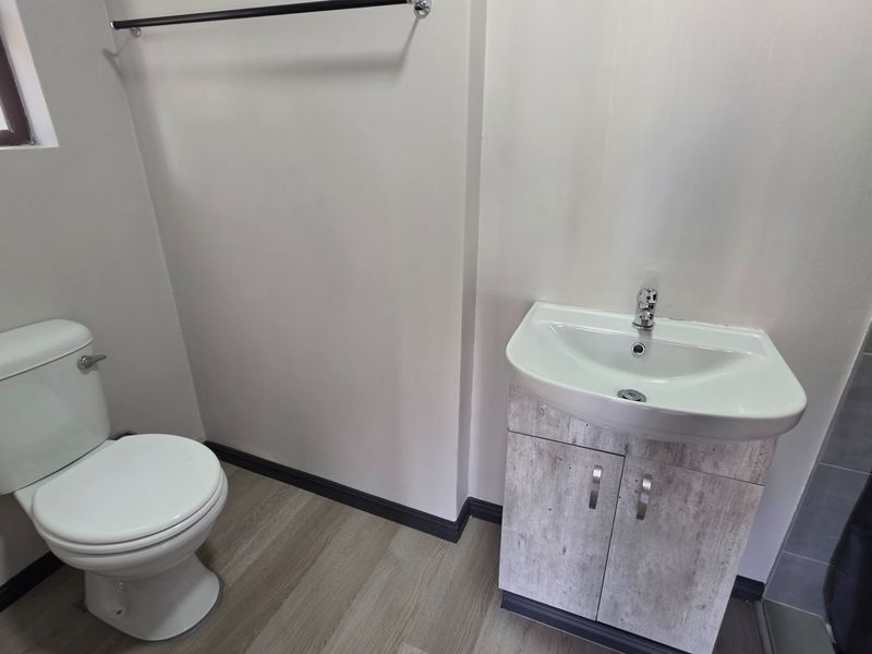 A clean and functional bathroom featuring a modern vanity cabinet, white washbasin, and toilet with wood-look vinyl flooring.