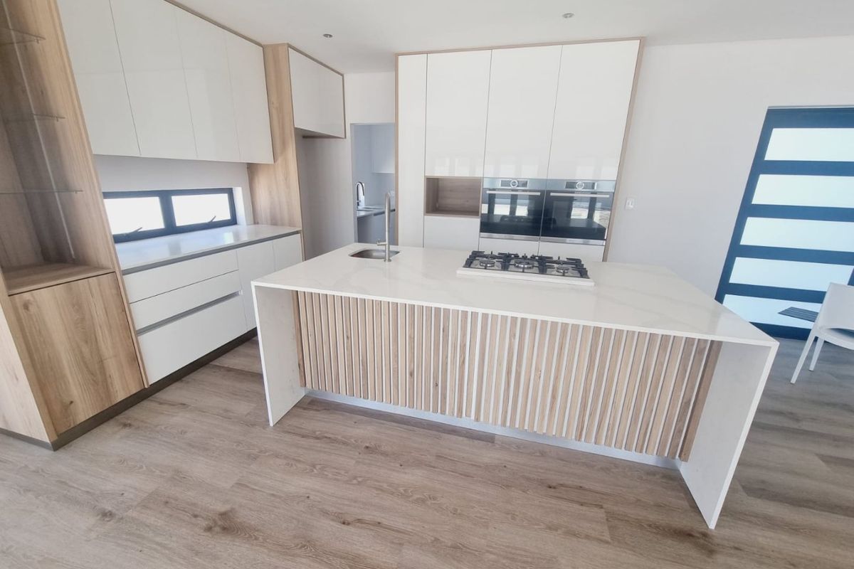 Modern kitchen featuring a central island with a gas hob, built-in ovens, sleek white cabinetry with wood accents, and durable laminate flooring.