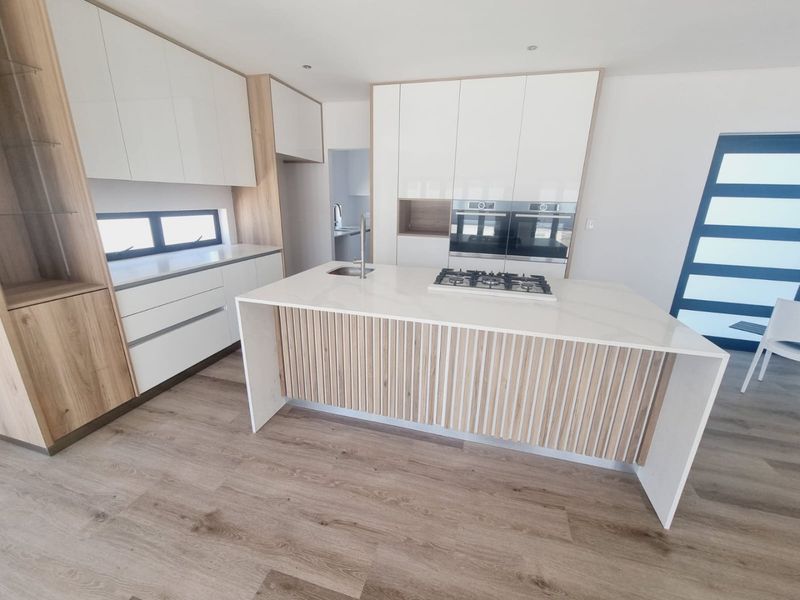 Modern kitchen featuring a central island with a gas hob, built-in ovens, sleek white cabinetry with wood accents, and durable laminate flooring.