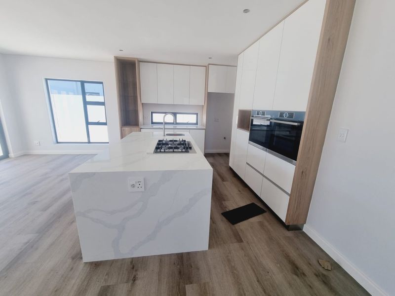 Modern open-plan kitchen featuring a large stone-topped island, built-in gas hob, integrated oven, and sleek cabinetry with wood-grain accents.
