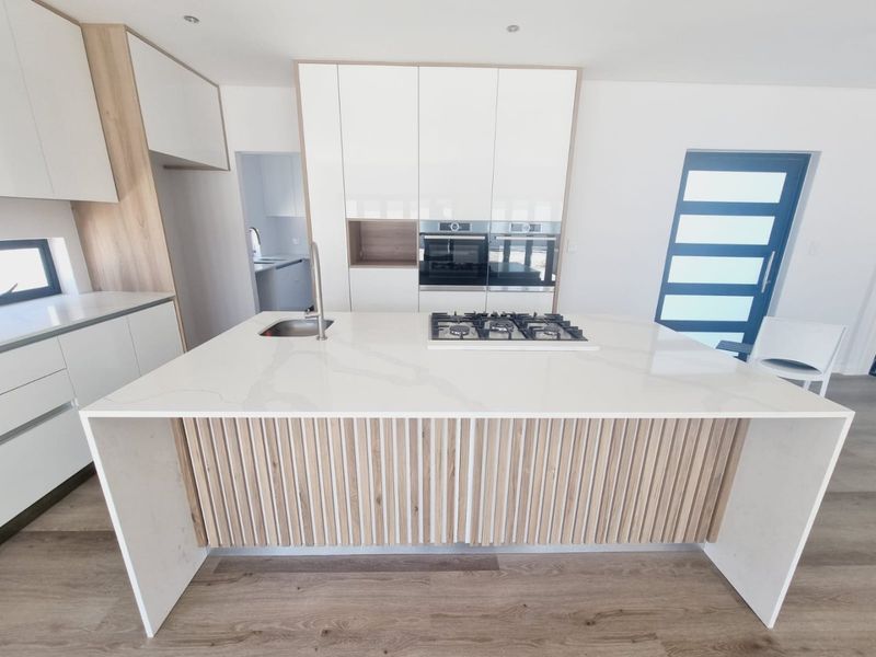 Modern kitchen featuring a large island with stone countertops, gas cooktop, integrated sink, and sleek white cabinetry with wood-look accents.