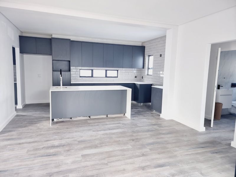 Modern open-plan kitchen featuring dark grey cabinetry, white countertops, subway tile backsplash, and light wood-look laminate flooring in a newly renovated space.