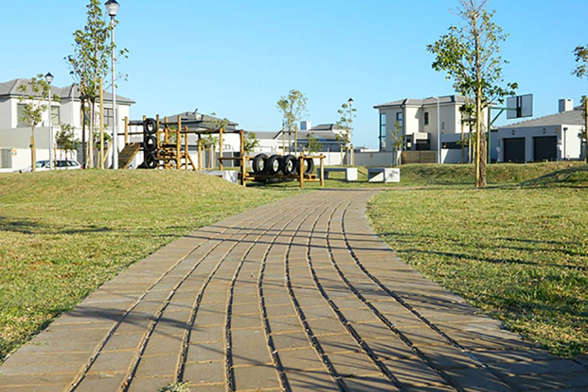 A well-maintained communal garden area featuring a paved walkway, playground equipment, and a basketball hoop within a residential estate setting.