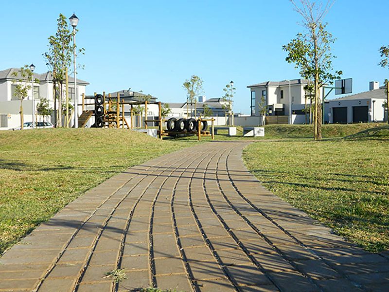 A well-maintained communal garden area featuring a paved walkway, playground equipment, and a basketball hoop within a residential estate setting.