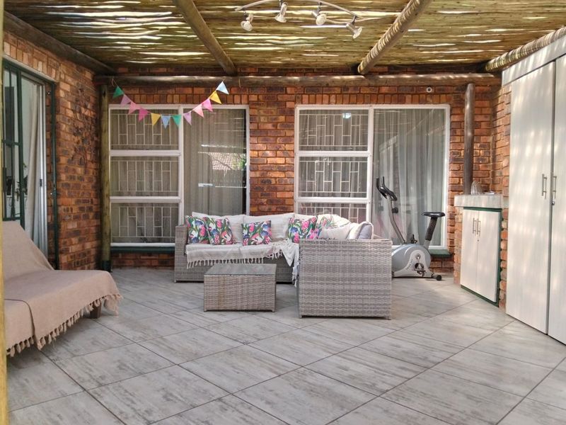 Covered patio area featuring exposed brick walls, tiled flooring, and a rustic thatched roof, providing a versatile outdoor living space.