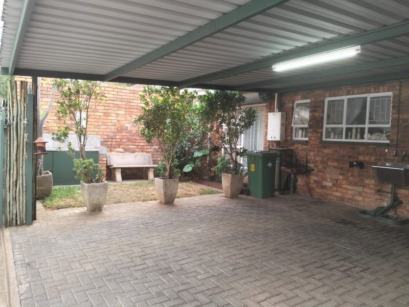 A covered carport area featuring brick paving, exposed brick walls, a utility sink, and a wall-mounted gas geyser.