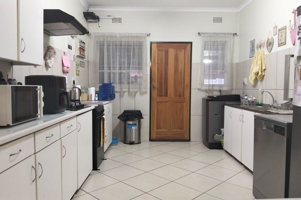 Functional kitchen featuring tiled flooring, ample built-in cabinetry, tiled splashbacks, and a dedicated sink area with direct access to an exterior door.