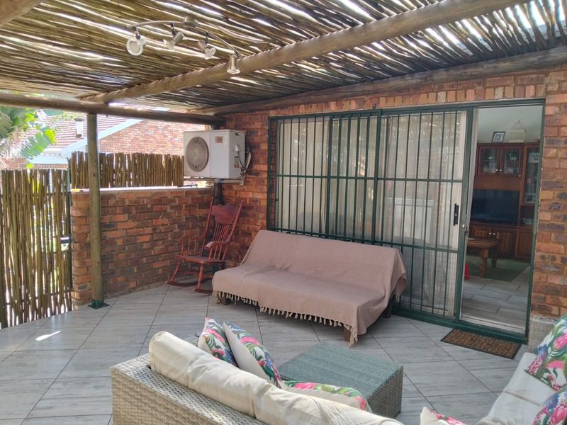 A covered patio area featuring a rustic thatched roof, exposed brick walls, and tiled flooring, providing a functional outdoor living space.