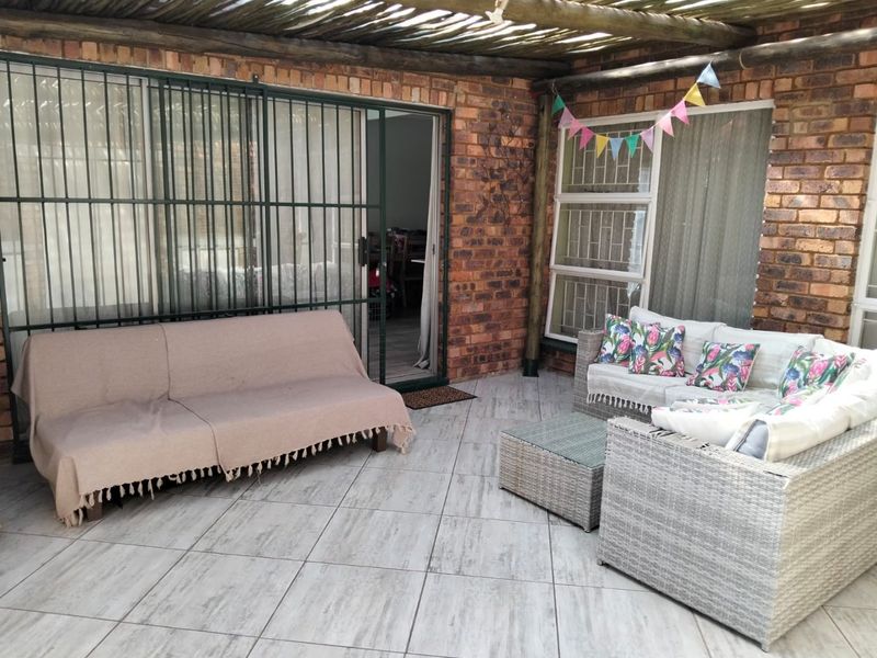 A covered patio area featuring exposed brick walls, tiled flooring, and a timber pergola roof, providing a functional outdoor living space.