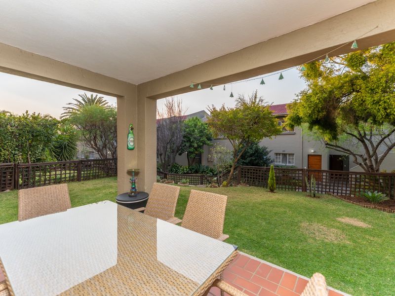 A covered patio area overlooking a private garden with established trees and wooden perimeter fencing, providing a pleasant outdoor living space.
