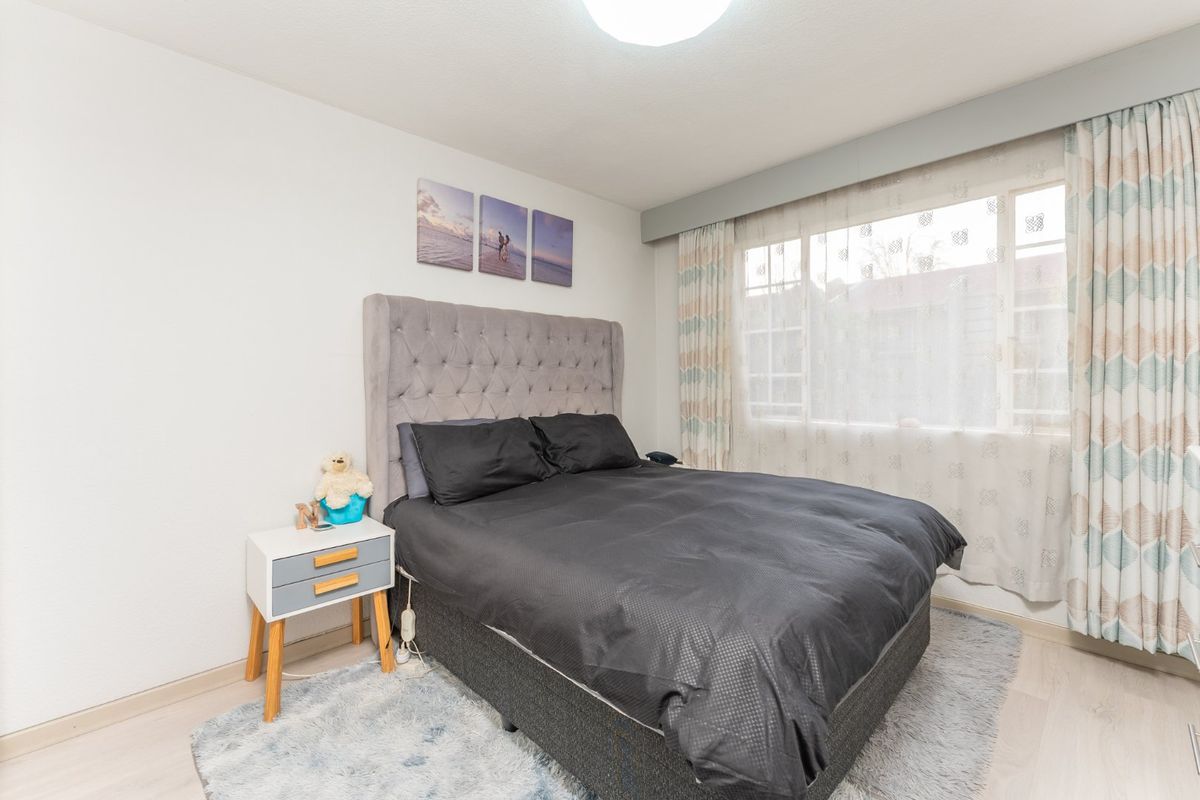 A well-lit bedroom featuring laminate flooring and a large window with installed curtain tracks, providing a neutral base for personalization.