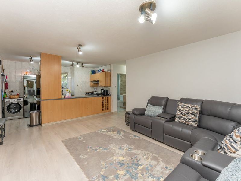 Open-plan living area featuring a functional kitchen with breakfast bar, integrated laundry space, and light laminate flooring throughout.