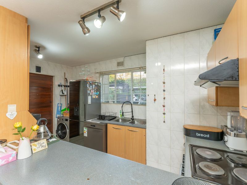 Functional kitchen featuring laminate cabinetry, tiled splashbacks, integrated hob with extractor, and a dedicated laundry area with plumbing connections.