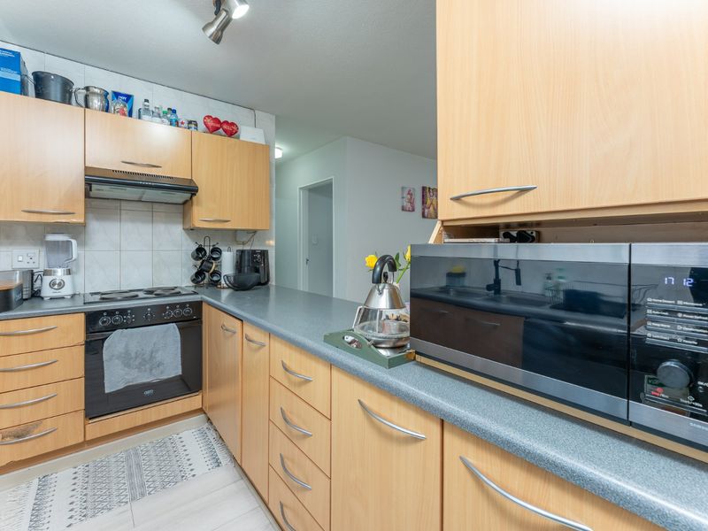 A functional kitchen featuring light wood-tone cabinetry, laminate countertops, a built-in oven, and an electric hob with an overhead extractor fan.