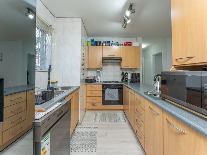 Functional kitchen featuring light wood-finish cabinetry, laminate countertops, built-in oven with extractor fan, and tiled splashbacks in a practical U-shaped layout.