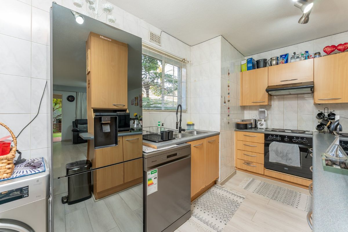 Functional kitchen featuring light wood cabinetry, built-in oven with extractor fan, double sink, and tiled splashbacks, offering a practical layout for daily use.