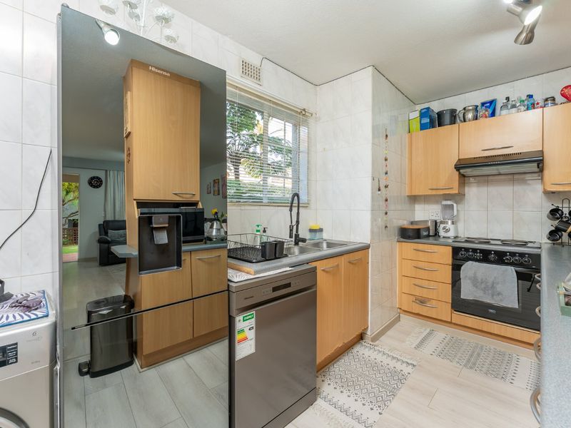 Functional kitchen featuring light wood cabinetry, built-in oven with extractor fan, double sink, and tiled splashbacks, offering a practical layout for daily use.