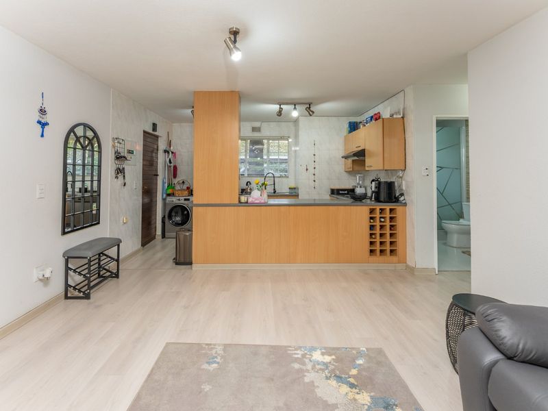 Open-plan living area featuring a functional kitchen with wood-finish cabinetry, integrated wine storage, and light laminate flooring throughout.
