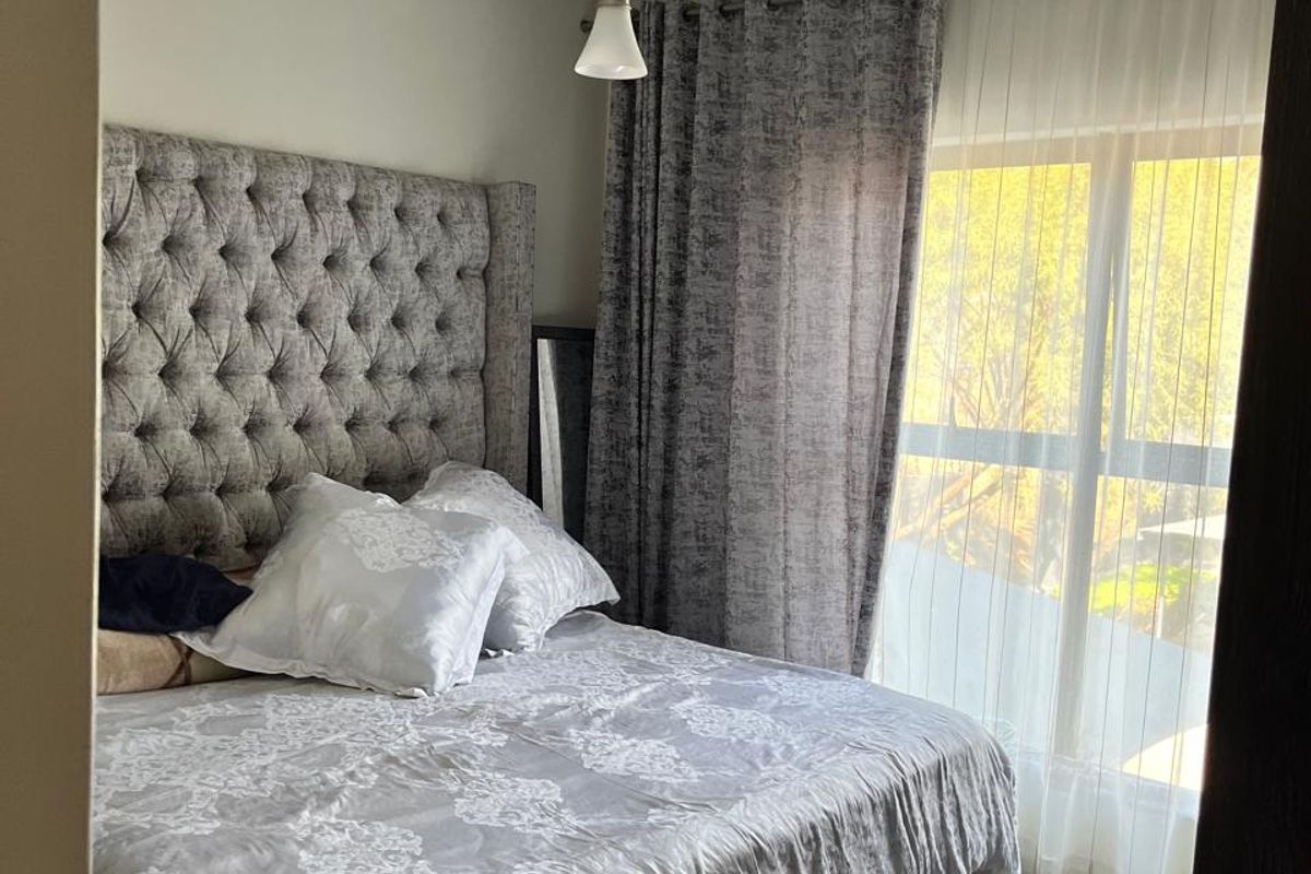 A well-lit bedroom featuring a large window with curtain tracks and a central pendant light fixture.