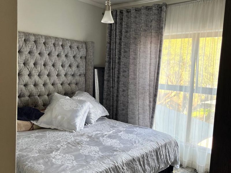 A well-lit bedroom featuring a large window with curtain tracks and a central pendant light fixture.