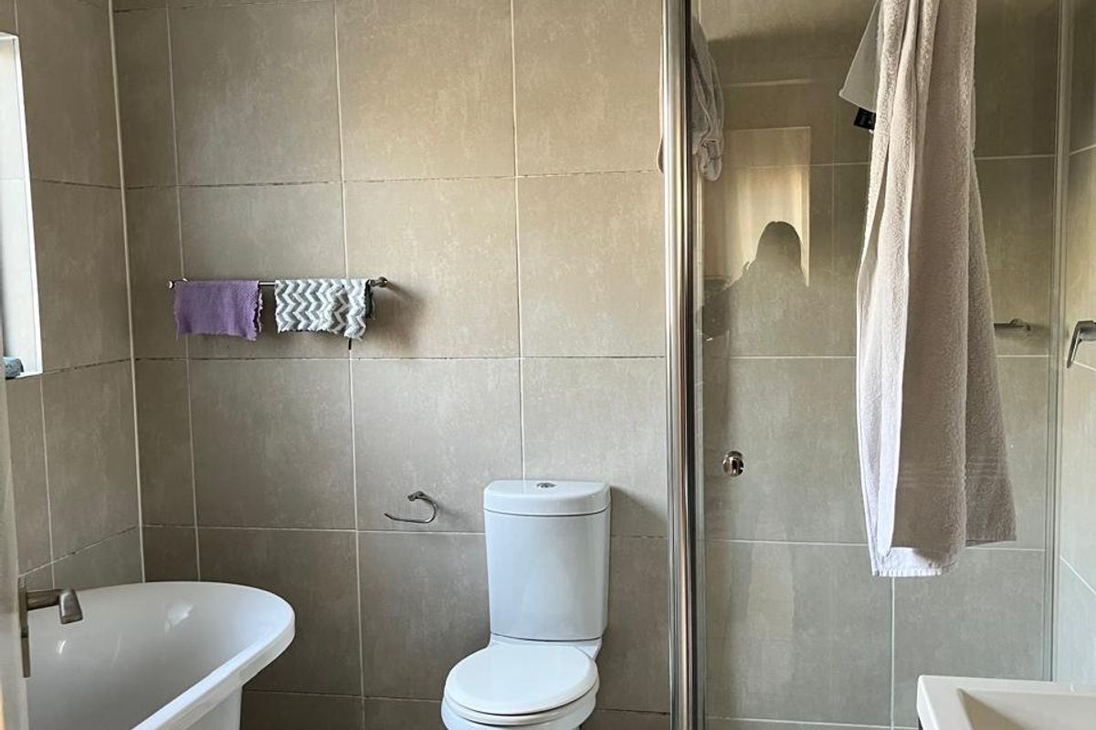 A functional bathroom featuring a freestanding bathtub, separate shower enclosure, toilet, and vanity basin with neutral wall and floor tiling.