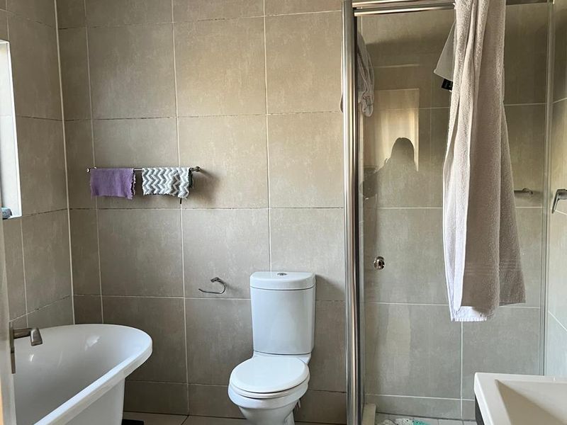 A functional bathroom featuring a freestanding bathtub, separate shower enclosure, toilet, and vanity basin with neutral wall and floor tiling.