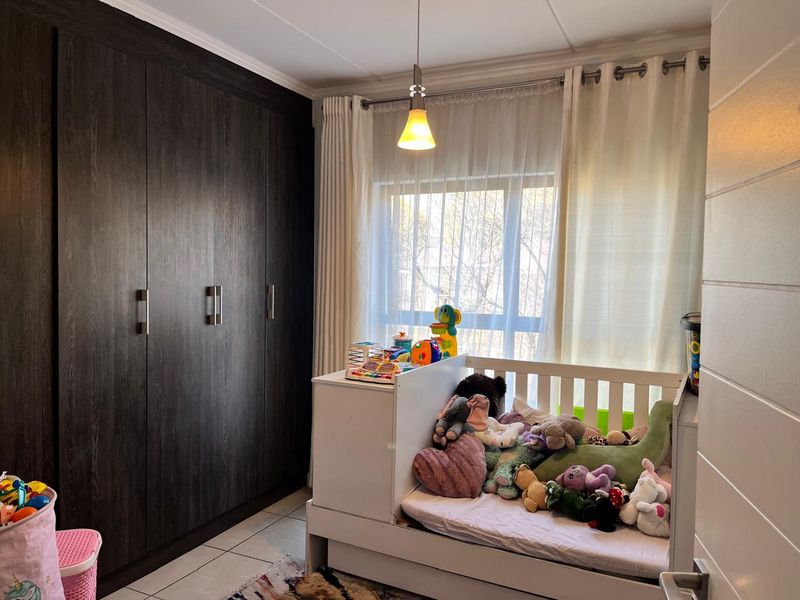 A bedroom featuring dark wood-finish built-in cupboards, tiled flooring, and a window with curtain fittings.