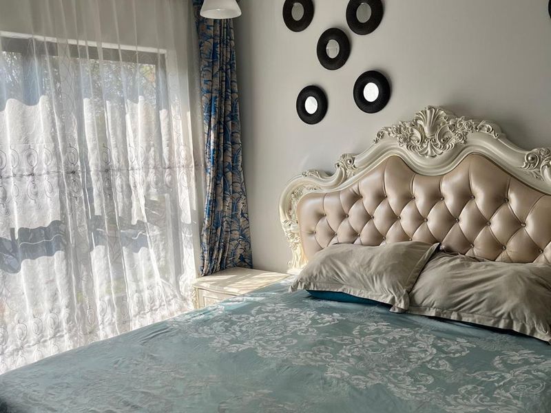 A well-lit bedroom featuring a sliding glass door with sheer curtains, coved ceiling details, and a central pendant light fixture.