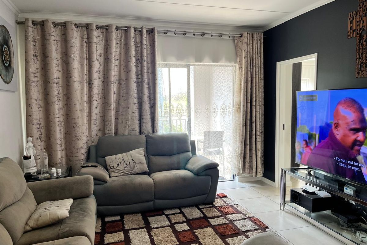A comfortable living room featuring tiled flooring, a coved ceiling, and a sliding glass door providing access to an outdoor balcony area.