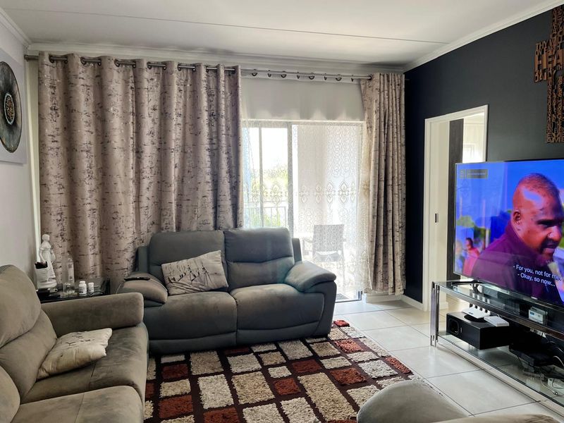 A comfortable living room featuring tiled flooring, a coved ceiling, and a sliding glass door providing access to an outdoor balcony area.
