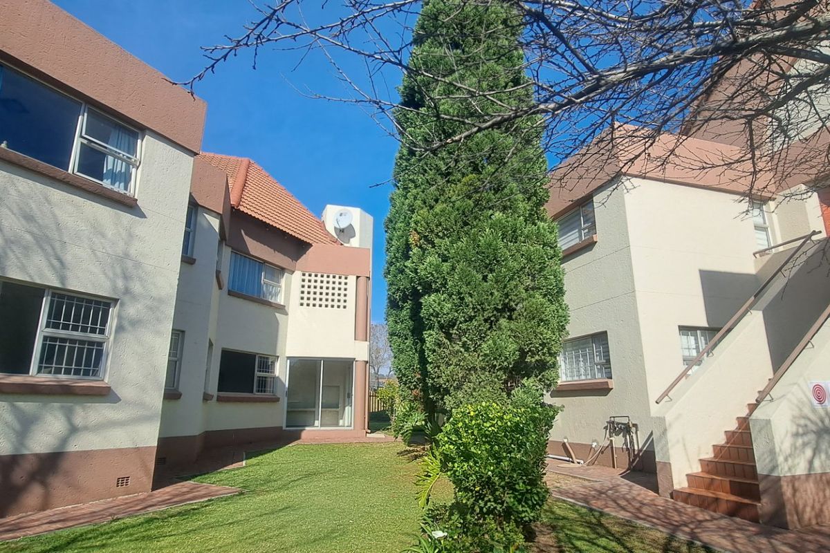 Rear view of a townhouse complex featuring a shared garden, paved walkways, external staircases, and multi-story residential units with stucco finishes.