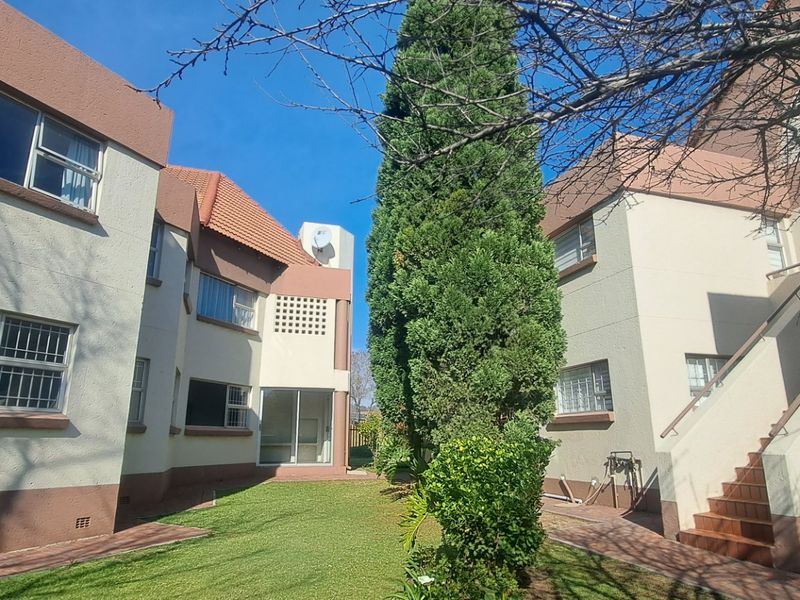 Rear view of a townhouse complex featuring a shared garden, paved walkways, external staircases, and multi-story residential units with stucco finishes.