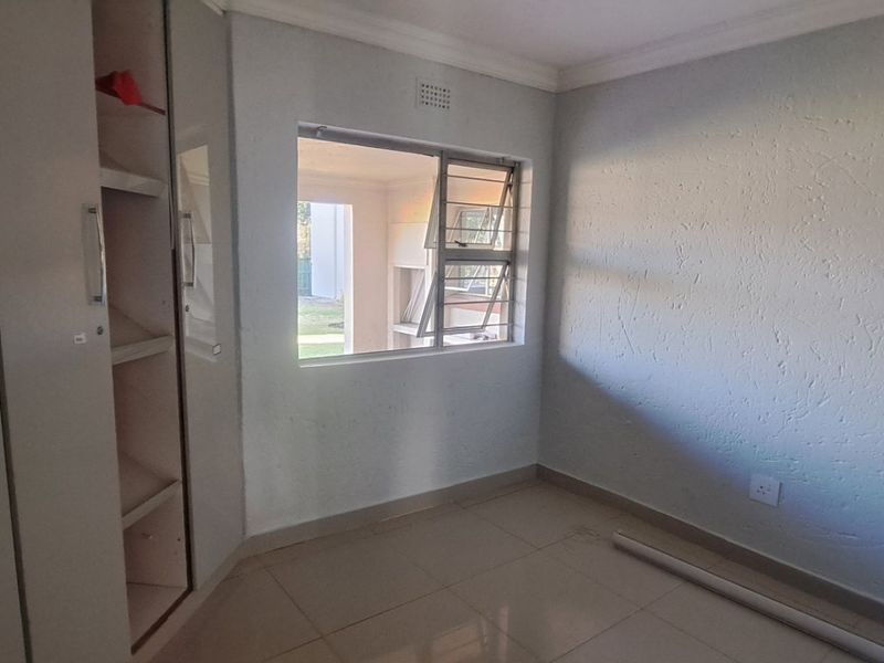 A vacant bedroom featuring built-in cupboards, tiled flooring, and a window with an exterior view.
