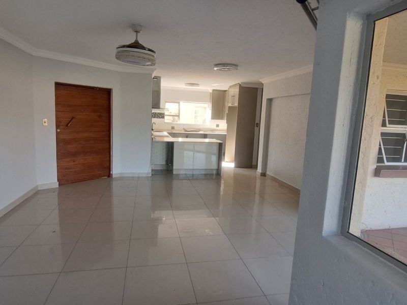 An open-plan living and kitchen area featuring neutral tiled flooring, modern cabinetry, and a kitchen island, offering a bright and spacious layout.