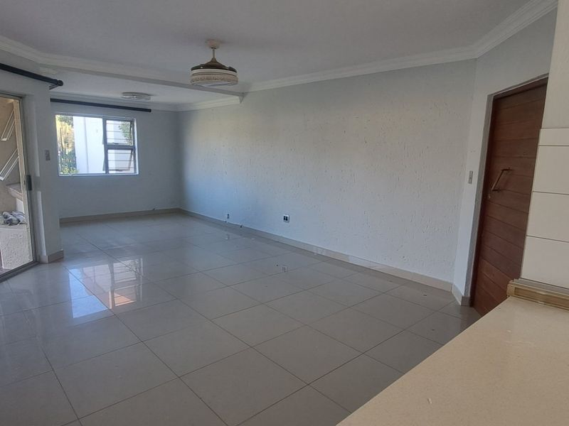 Spacious open-plan living area featuring large format floor tiles, a ceiling fan, and direct access to an outdoor patio through sliding glass doors.