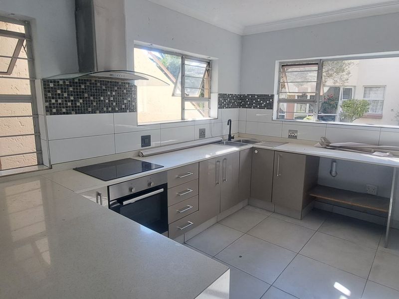 A functional kitchen featuring quartz countertops, built-in oven, electric hob, and tiled splashbacks, currently vacant and ready for final finishing touches.
