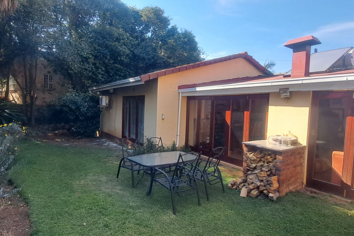 Rear exterior view of the house featuring a lawn, brick built-in braai, solar water heater, and timber sliding doors leading into the living area.