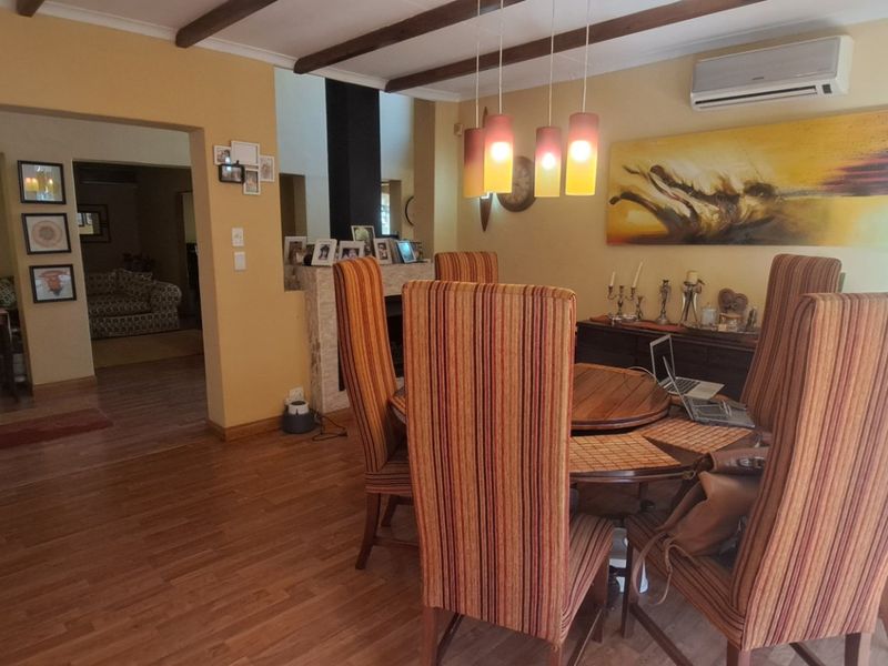 Dining room featuring exposed timber ceiling beams, laminate flooring, a stone-clad fireplace, and a wall-mounted split-system air conditioning unit.