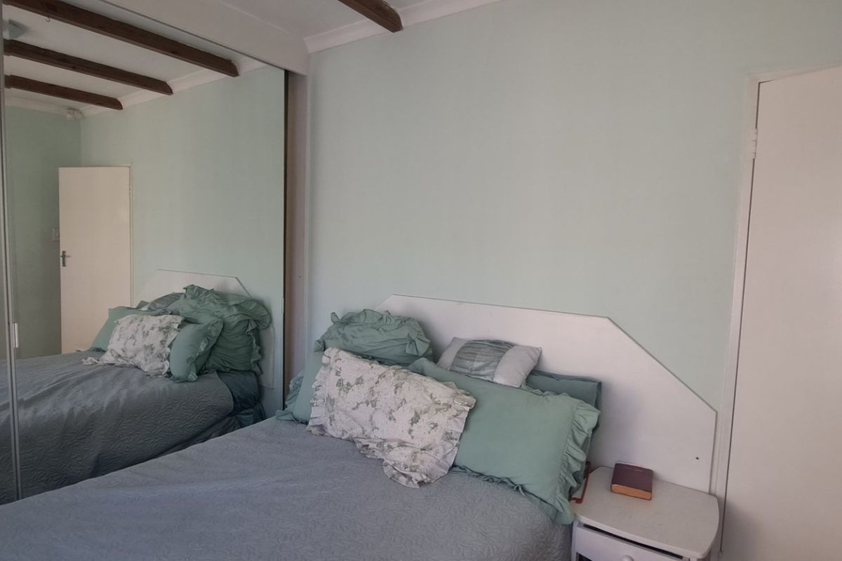 A bedroom featuring exposed ceiling beams, a built-in wardrobe with mirrored sliding doors, and a wall-mounted split-system air conditioner.