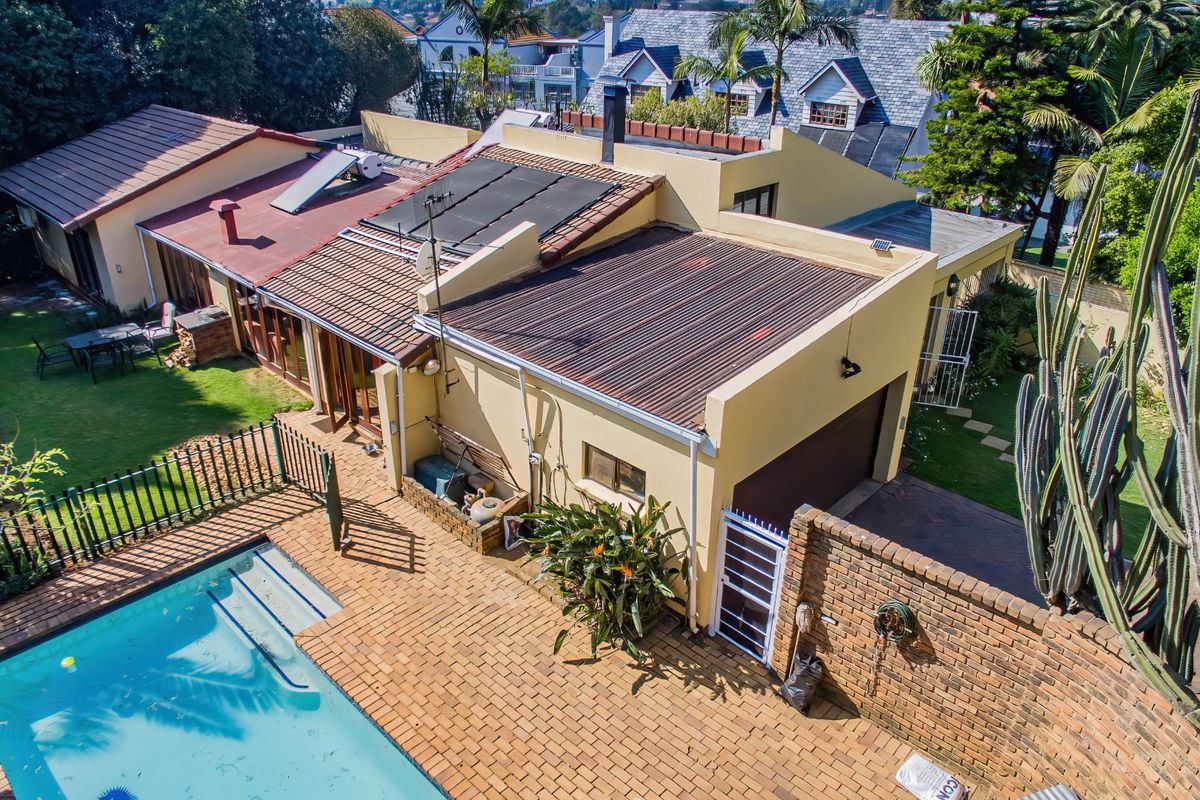 Aerial view of the property featuring a swimming pool, brick paved patio area, garage, and various roof sections including solar water heating panels.