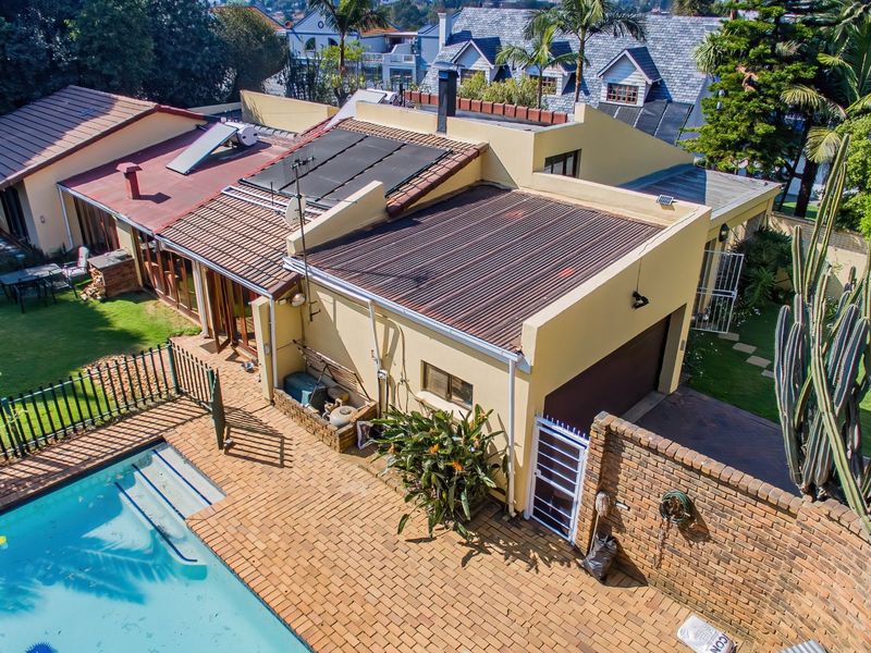 Aerial view of the property featuring a swimming pool, brick paved patio area, garage, and various roof sections including solar water heating panels.