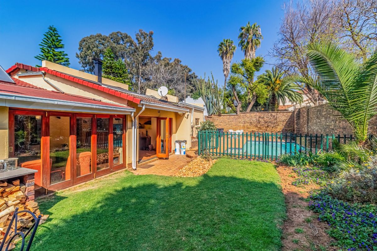 Rear view of the property featuring a paved patio, landscaped garden, and a fenced swimming pool area with direct access via timber folding doors.