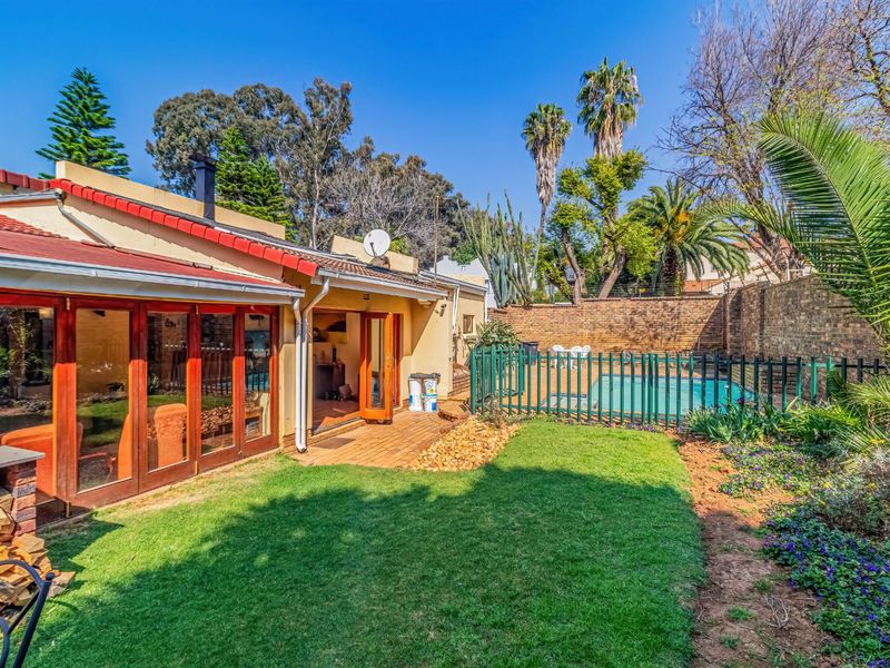 Rear view of the property featuring a paved patio, landscaped garden, and a fenced swimming pool area with direct access via timber folding doors.
