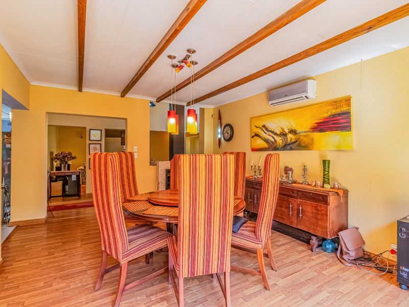 Dining room featuring exposed timber ceiling beams, laminate wood flooring, and a wall-mounted split-system air conditioning unit.