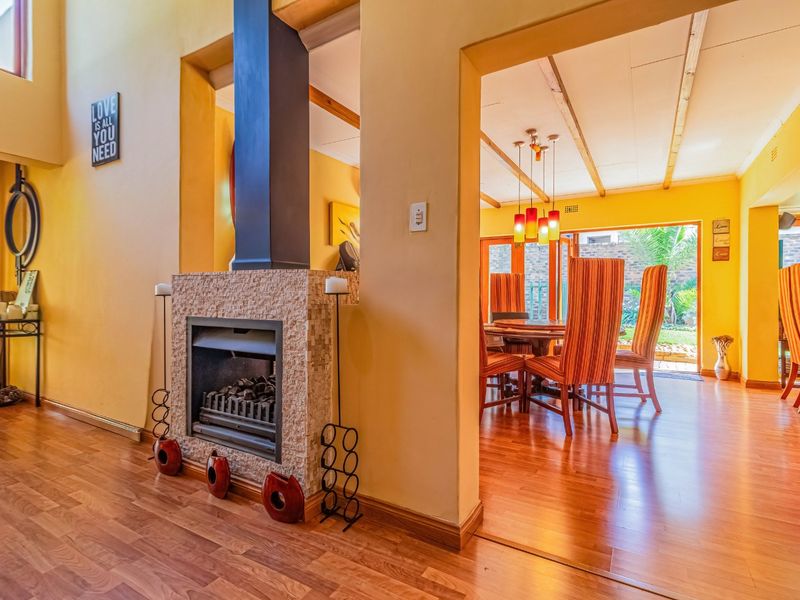 Open plan living and dining area featuring a stone-clad fireplace, laminate flooring, exposed ceiling beams, and direct access to the garden through sliding doors.