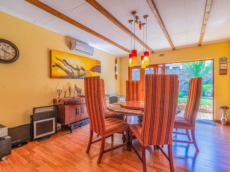 Dining room featuring exposed timber ceiling beams, laminate flooring, and folding glass doors providing direct access to the rear garden area.