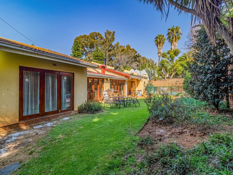 Rear view of the house featuring a lawn, garden beds, and wooden folding doors leading to the interior living spaces.