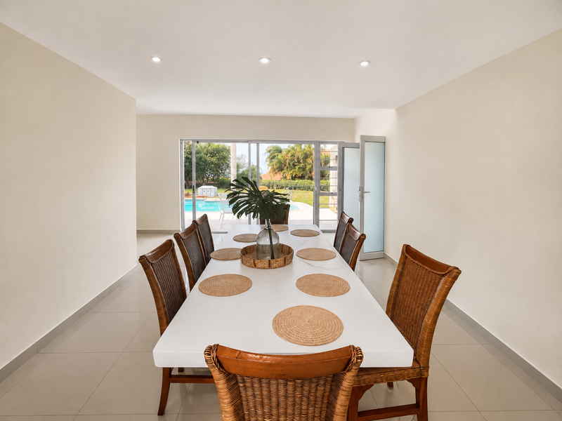 A bright dining room featuring neutral tiled flooring, recessed lighting, and large sliding glass doors providing direct access to the outdoor pool area.